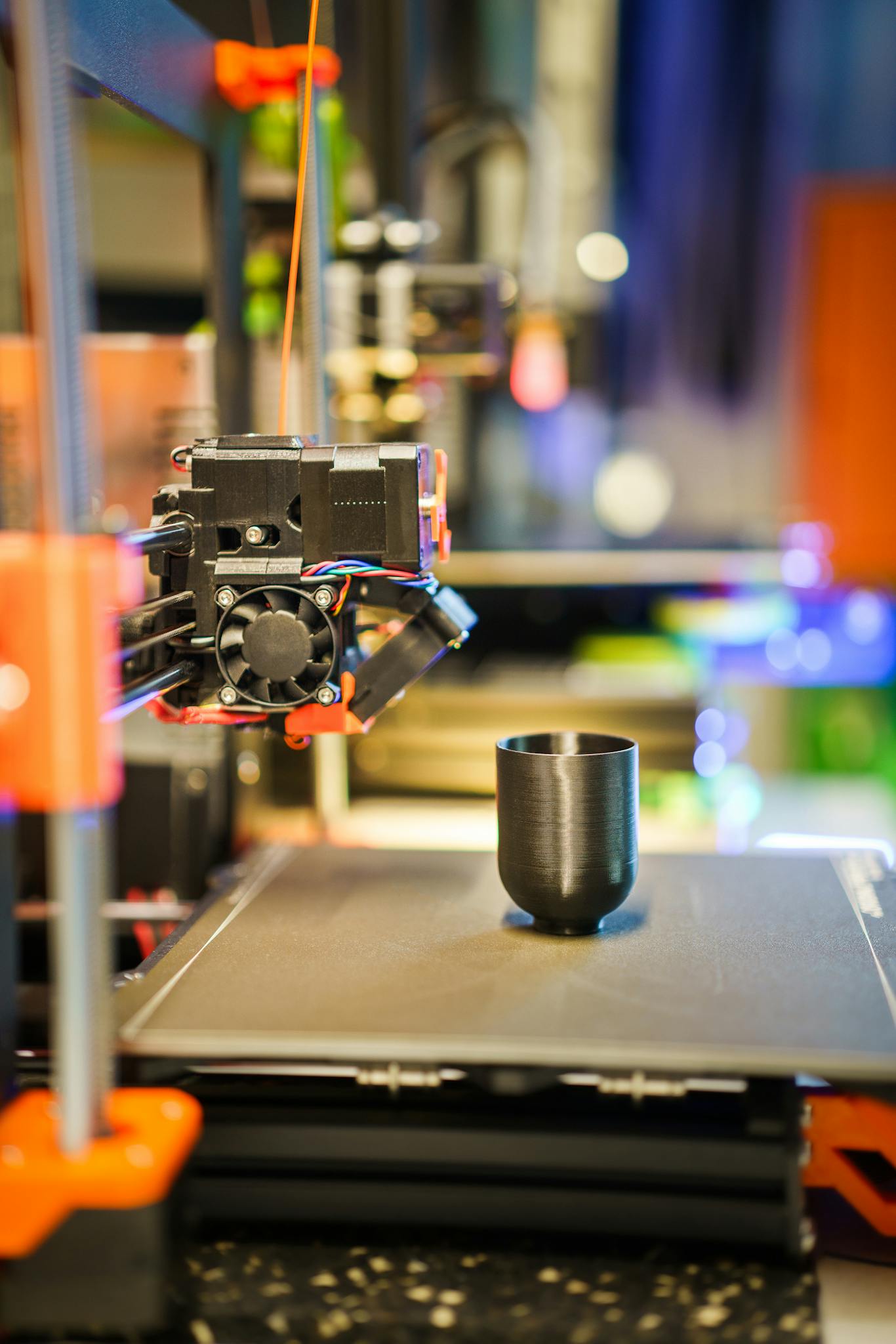 Detailed shot of a 3D printer manufacturing a black plastic cup indoors.